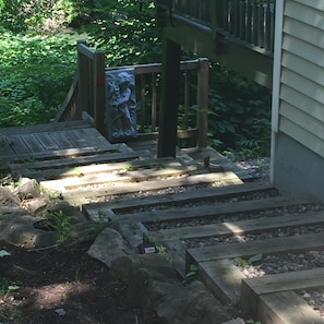 A wooden staircase leading to a porch with a statue, surrounded by greenery. - PRISTINE CAPE COD ON THE CREEK! 4 Large Bedrooms - 6 Guests! (Albany)