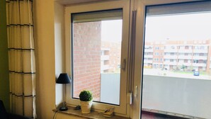 Una habitación con un radiador, una planta en maceta, una lámpara y vistas a un edificio de ladrillo y una calle a través de una ventana.