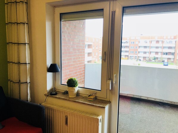 A room with a radiator, a potted plant, a lamp, and a view of a brick building and a street through a window.