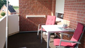 Un patio con pared de ladrillo, una mesa, dos sillas y un paraguas verde.