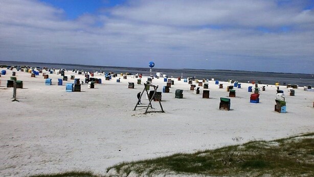 Una playa con numerosos contenedores de colores dispersos sobre la arena.