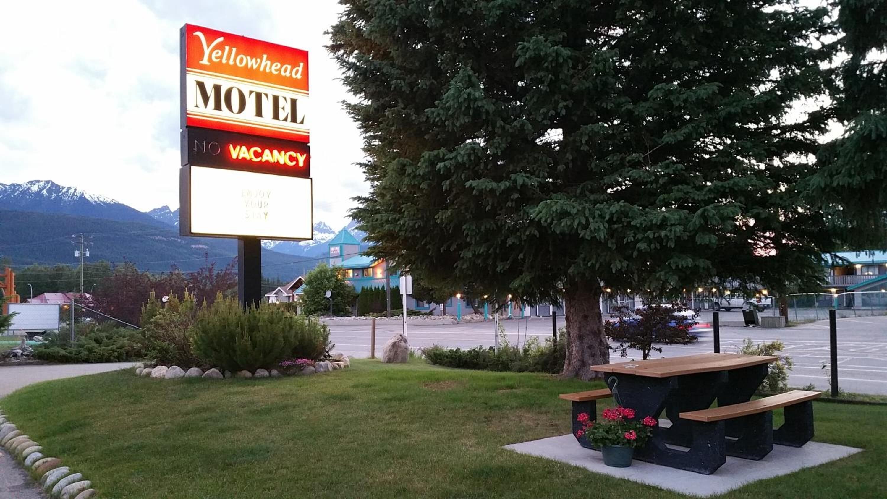 Placa de motel com aviso de quartos disponíveis, mesa de piquenique com flores e montanhas ao fundo.
