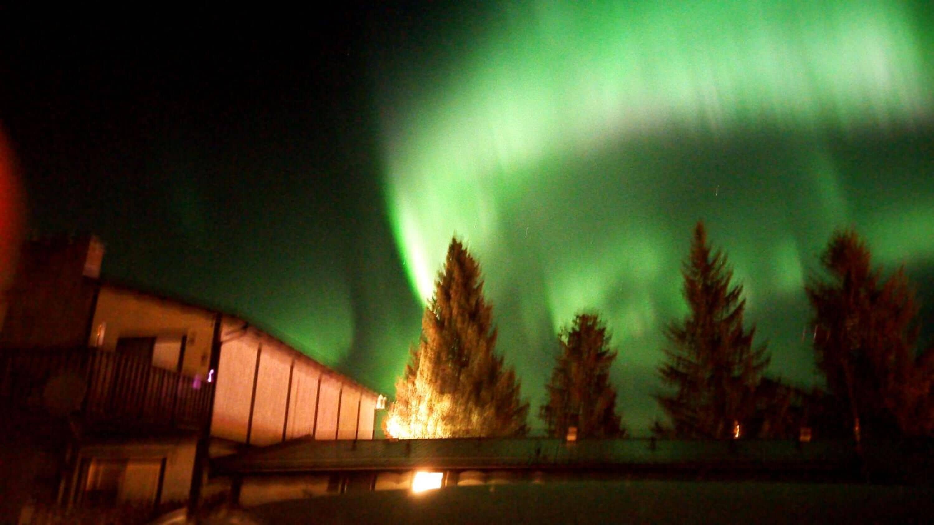 A building with a large, illuminated structure, possibly a hotel, with a view of the northern lights in the background.