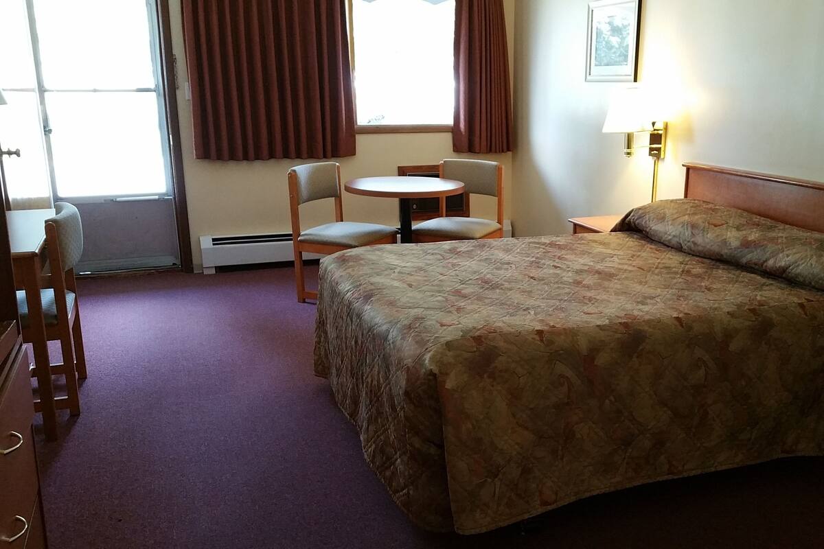 Una habitación de hotel con cama, escritorio, silla, mesita y lámpara.