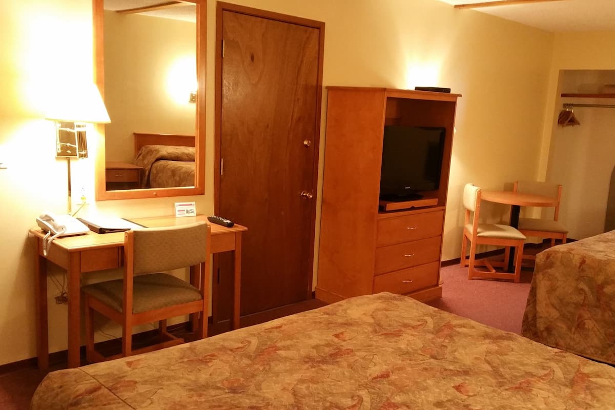 Habitación de hotel con escritorio, silla, dos camas, televisión y armario.