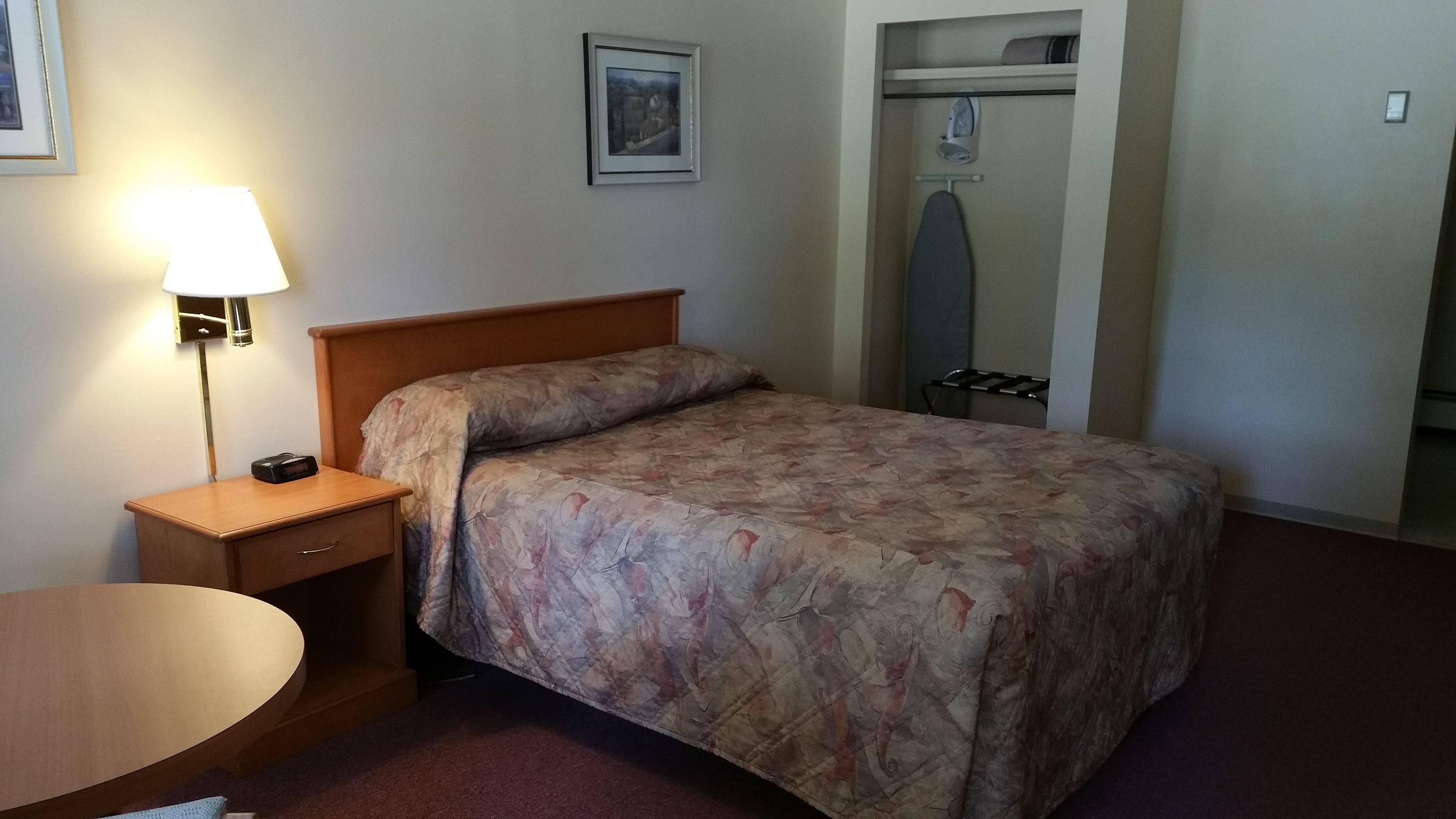 A neatly made bed with a floral bedspread, a bedside lamp, a wooden nightstand, and a closet with hanging clothes.