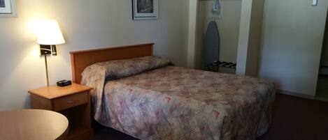 A neatly made bed with a floral bedspread, a bedside lamp, a wooden nightstand, and a closet with hanging clothes.
