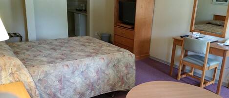 A hotel room with a bed, a desk with a chair, a television, and a wardrobe.