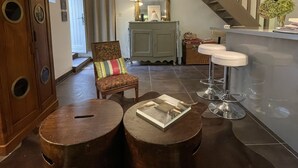 A spacious living area with a wooden cabinet, a cushioned chair, a small round table with a book, and a bar area with stools. - Charming old quiet house with garden - Village and sea on foot (Arradon)