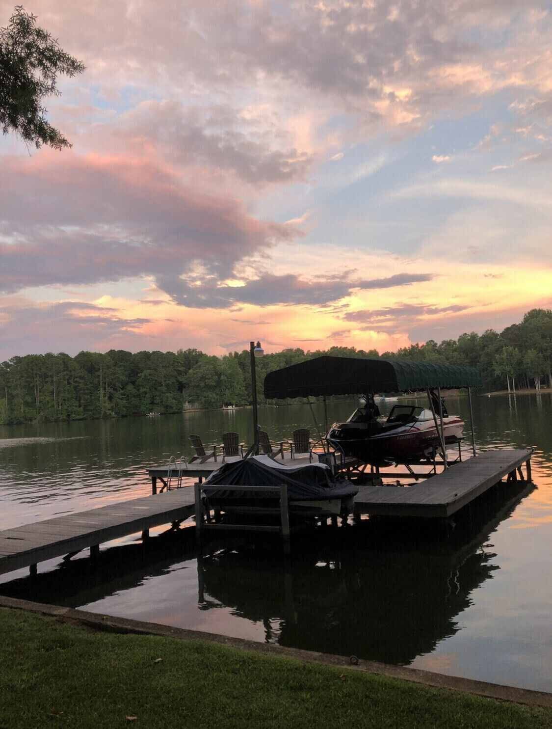 A dock with a covered seating area, a boat, and a calm lake at sunset.