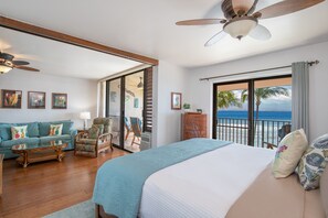 Habitación amplia con una cama grande, un sofá y una silla. Tiene un balcón con vista al océano.