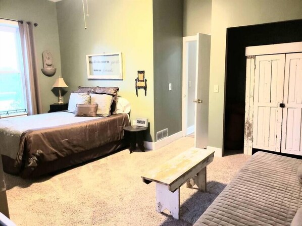 A bedroom with a bed, a bench, a nightstand, a lamp, a wall clock, and a door. - Beautiful, remodeled penthouse in Lebanon Ohio, between Dayton and Cincinnati (Lebanon)