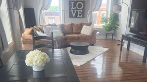 A living room with a brown sofa, a dining table with a vase of flowers, a ceiling fan, and a TV stand. - Beautiful, remodeled penthouse in Lebanon Ohio, between Dayton and Cincinnati (Lebanon)