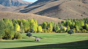 Un parcours de golf doté d’un club-house, entouré de collines et d’arbres.