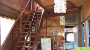 Un interior de madera con una escalera de madera, un refrigerador y un armario con vajilla.