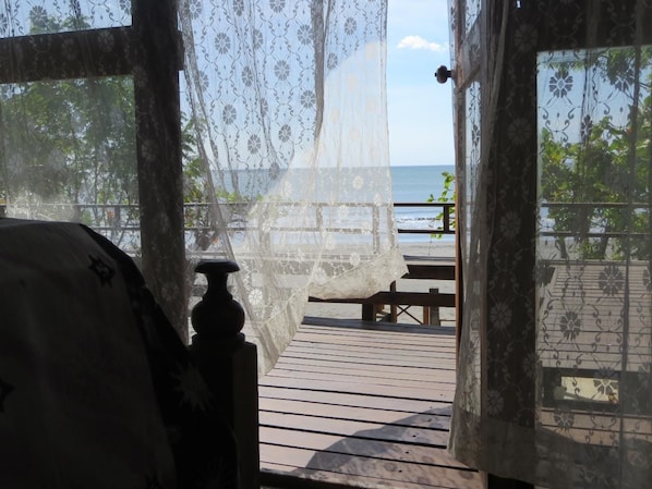 Une terrasse en bois avec un banc, une moustiquaire et une vue sur la mer.