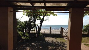 Un espacio al aire libre cubierto con una mesa y sillas, vista a la playa y un árbol.