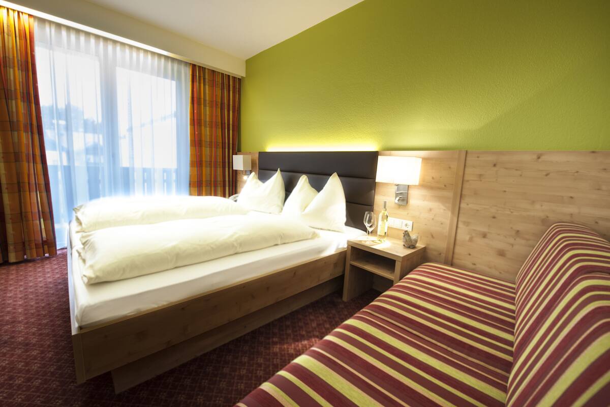 Ein Hotelzimmer mit einem großen Bett, einem Nachttisch mit einer Lampe und einem gestreiften Sofa.