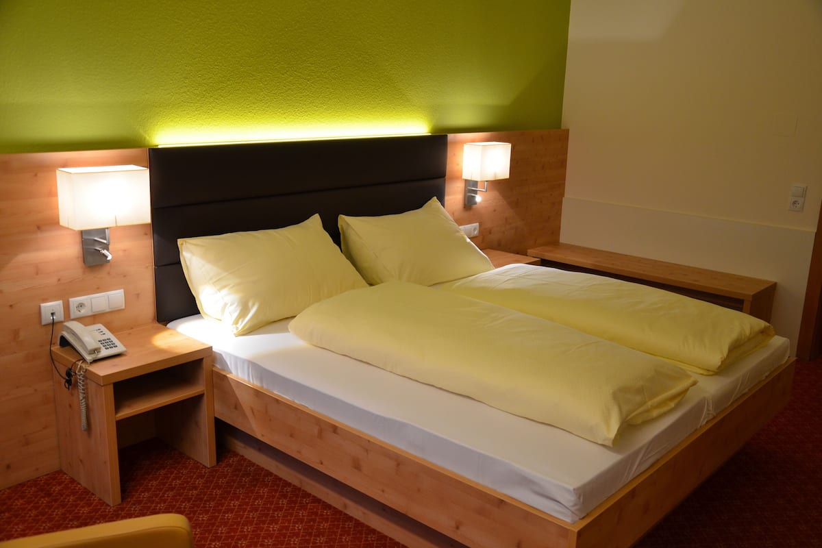 Ein Bett mit Holzkopfteil, zwei Nachttischlampen, ein Nachttisch mit Telefon und ein roter Teppichboden.