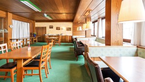 Ein Restaurant mit Holztischen und -stühlen, einem grünen Teppich und Pendelleuchten.