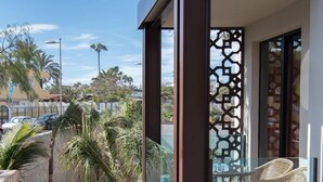 A balcony with wicker chairs, a glass railing, and a view of a sandy area with palm trees. - Alhambra Boutique  (San Bartolomé de Tirajana)