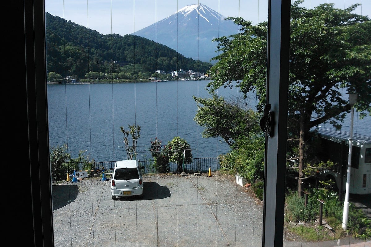 A view of a lake with a mountain in the background, a parking area with a car, and a building with a fence in the foreground.