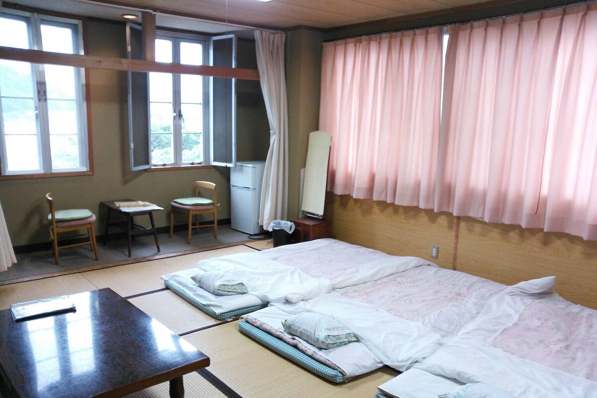 A traditional Japanese room with tatami flooring, a futon bed, a wooden table, and a small desk.