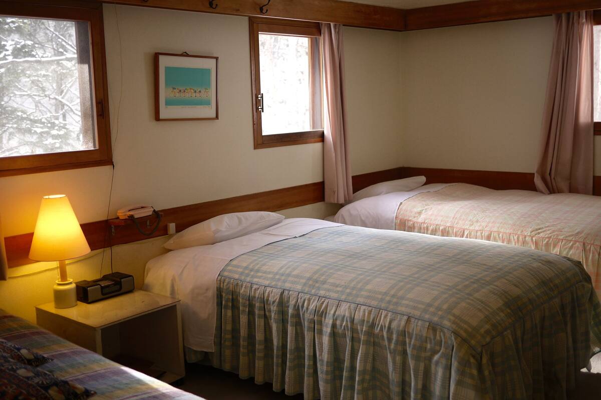 A room with two beds, a lamp, a framed picture on the wall, and a window with curtains.