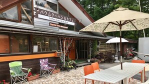 An outdoor seating area with tables and chairs, a large umbrella, and a building with a sign that reads "Coffee, Cake, B.B.Q. Pub". - Pension Tengallonhat (Matsumoto)