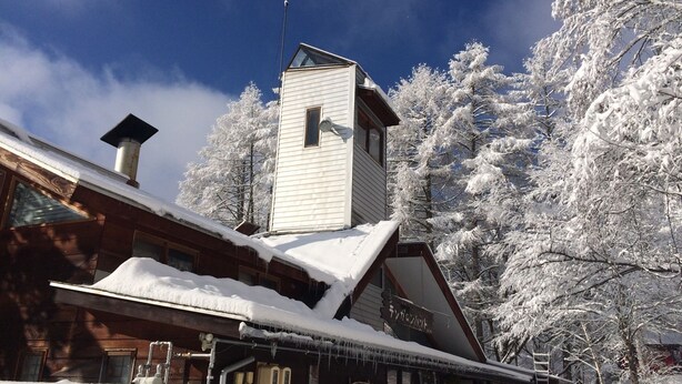 A wooden cabin with a small tower, snow-covered trees, and a clear blue sky. - Pension Tengallonhat (Matsumoto)