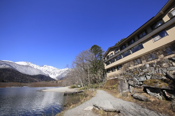 A lakeside hotel with a stone wall and a pathway leading to the water. - Taisyoike Hotel, Kamikochi (Matsumoto)
