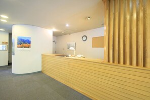 A reception area with a wooden reception desk, a clock on the wall, and a framed picture of a mountain landscape. - Taisyoike Hotel, Kamikochi (Matsumoto)