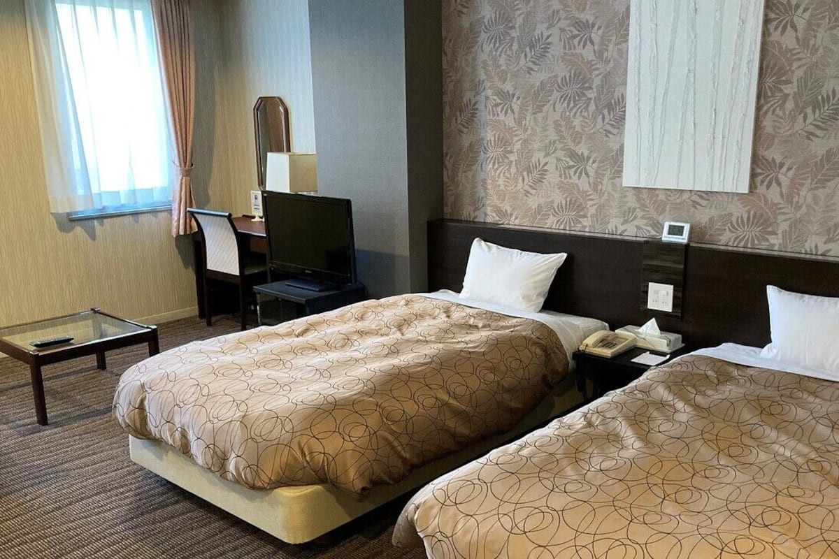 Habitación de hotel con dos camas, un escritorio, una silla, un televisor y una ventana con cortinas.