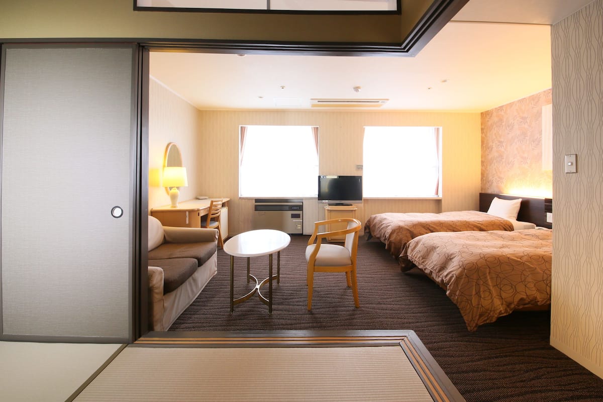 Habitación de hotel con cama, escritorio, silla, televisor y ventana.