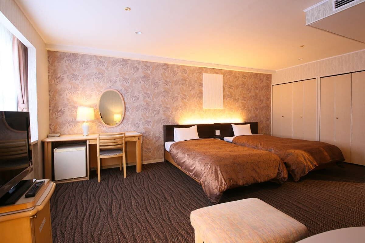 Una habitación de hotel con cama, escritorio, silla, televisor y armario.