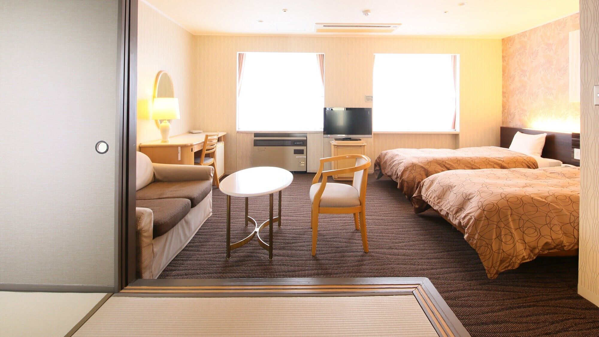 A hotel room with a sofa, a small round table, two single beds, a TV, and a window.