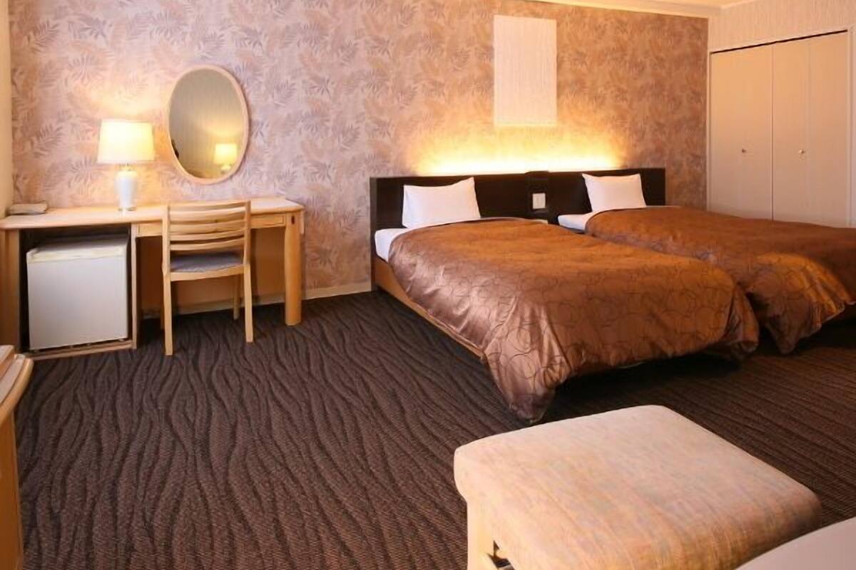 Una habitación de hotel con cama, escritorio con silla, espejo y armario.
