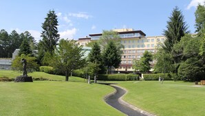 Un área verde bien cuidada con un sendero serpenteante, rodeada de árboles y un edificio de varios pisos al fondo.