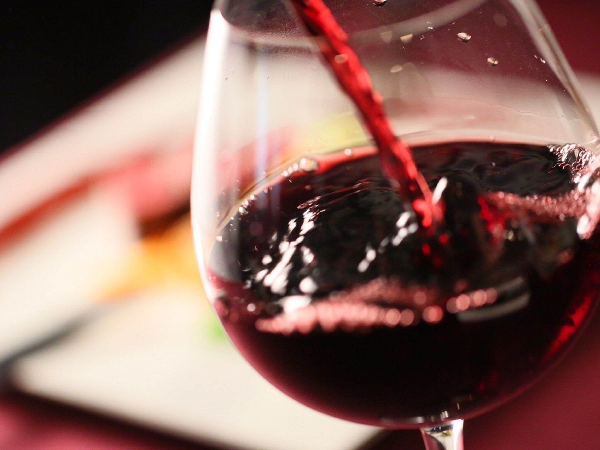 A close-up of a wine glass with red wine being poured into it.