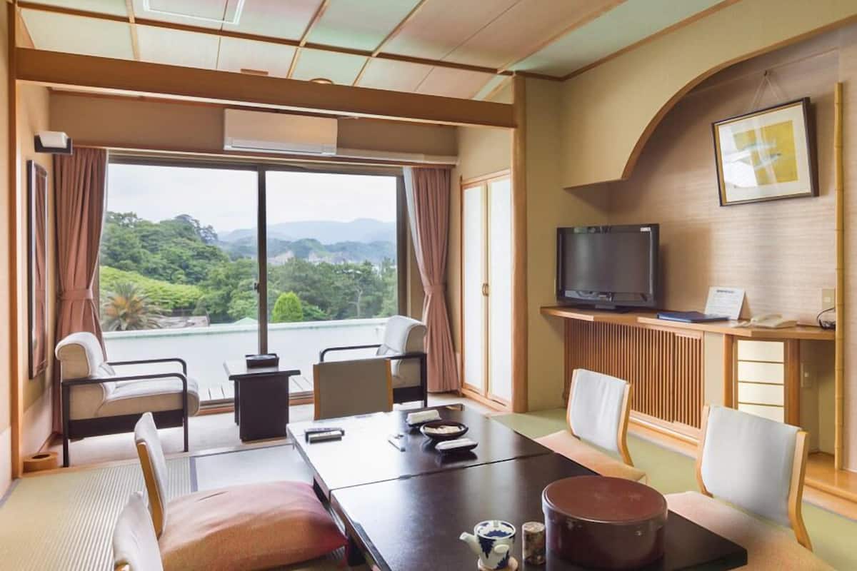 Une chambre d’hôtel dotée d’une grande table à manger, de chaises, d’un téléviseur et offrant une vue sur la verdure.