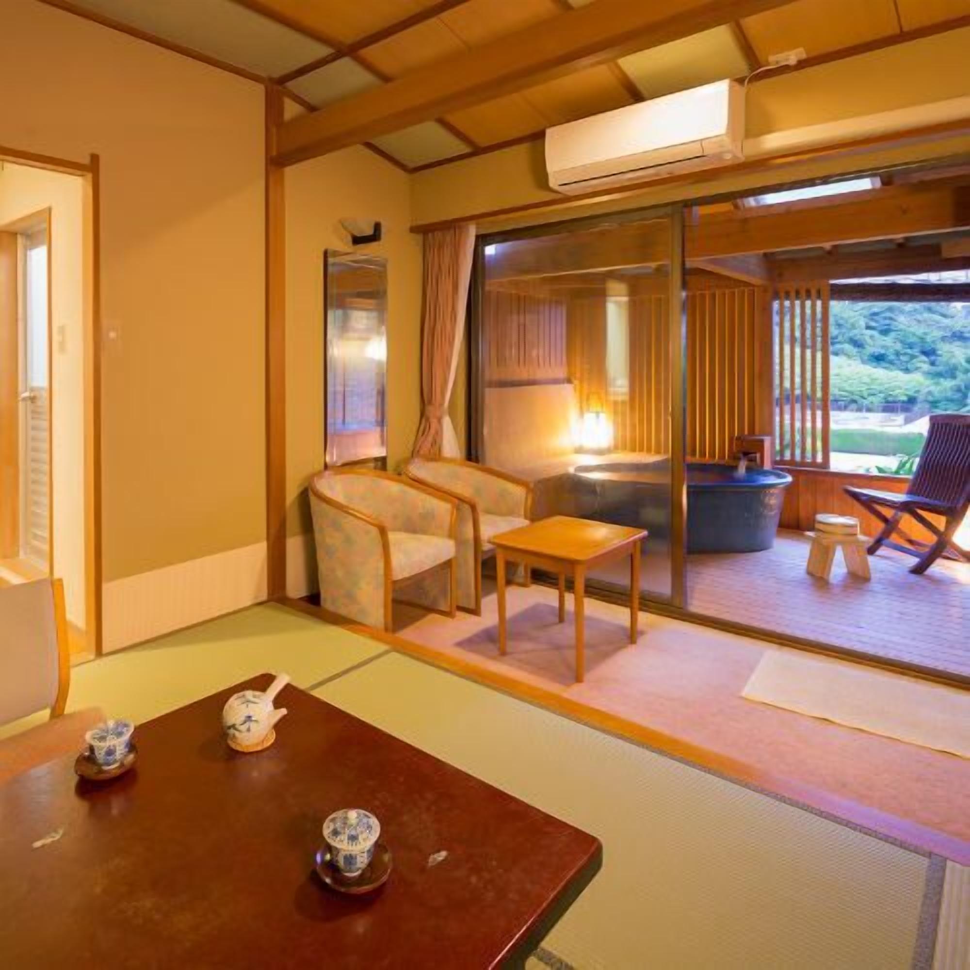 Una tradizionale stanza giapponese con pavimento in tatami, un tavolino con set da tè, una sedia e una porta scorrevole che si apre su un'area esterna.