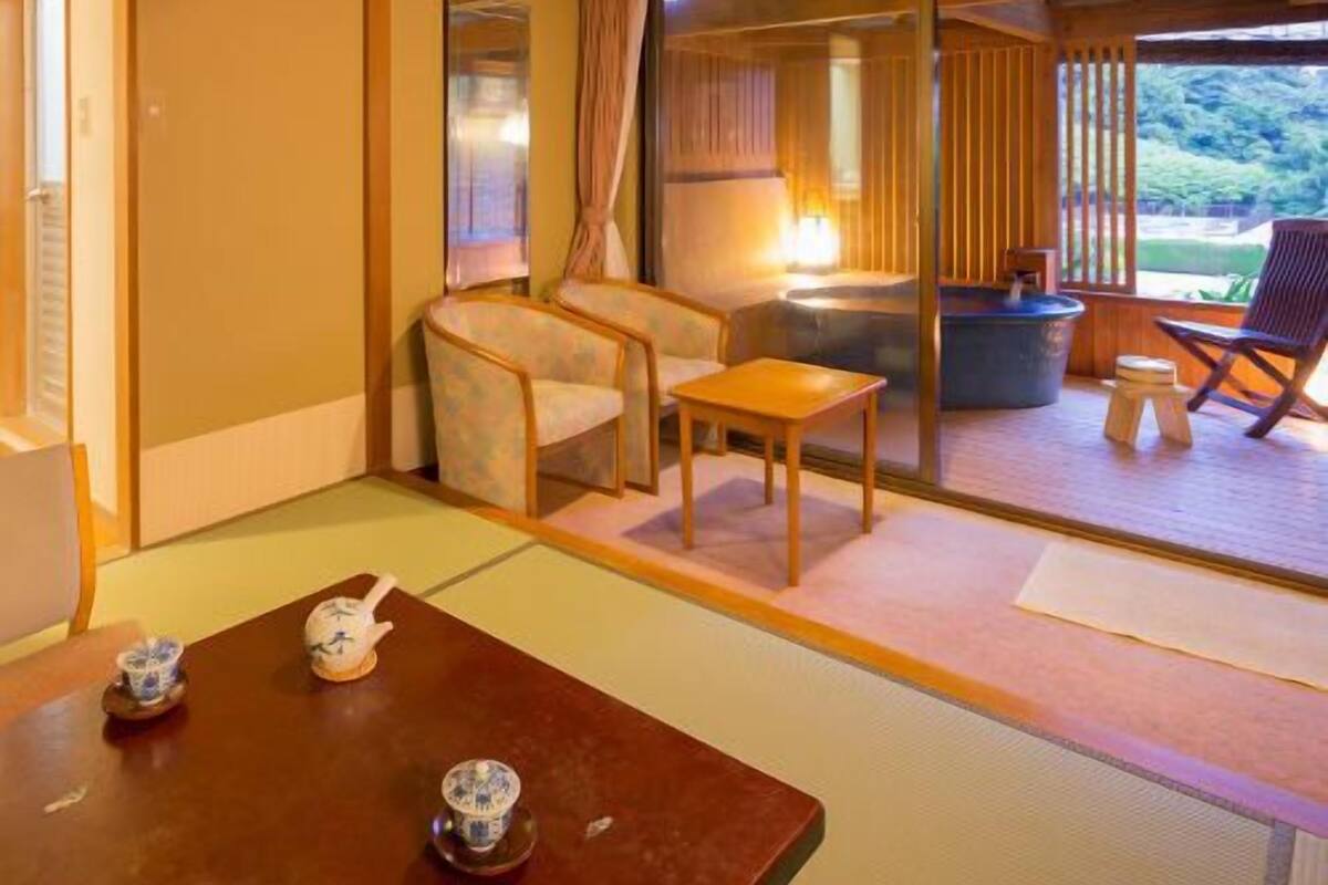 Une pièce de style japonais traditionnel, avec un sol recouvert de tatamis, une petite table sur laquelle sont disposés des accessoires pour la cérémonie du thé, une chaise et une porte coulissante donnant sur un espace extérieur.
