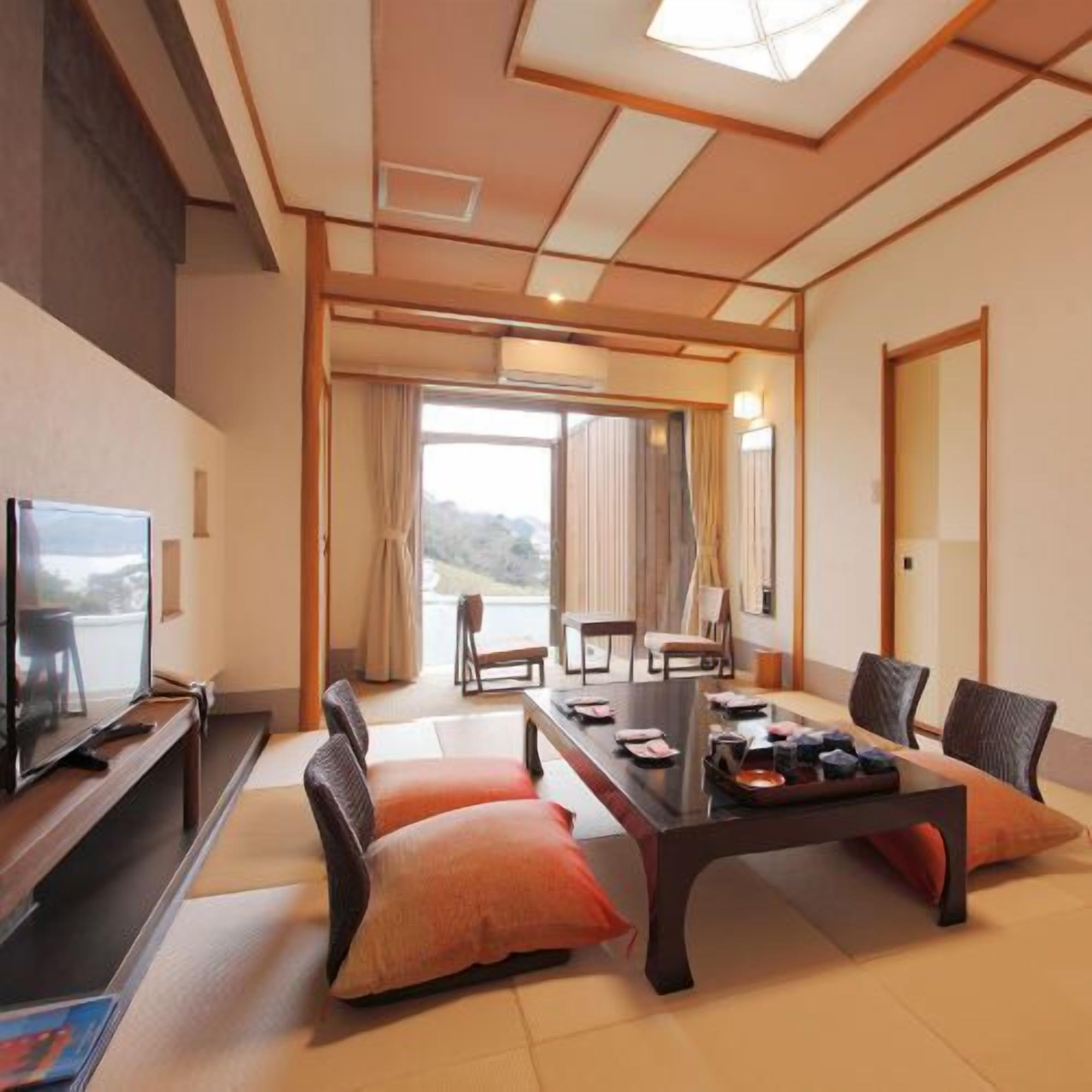 Una stanza tradizionale giapponese con pavimento in tatami, un tavolino con cuscini, un televisore e vista sull'esterno.