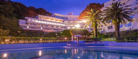 Un hotel moderno con piscina, rodeado de abundante vegetación y palmeras.