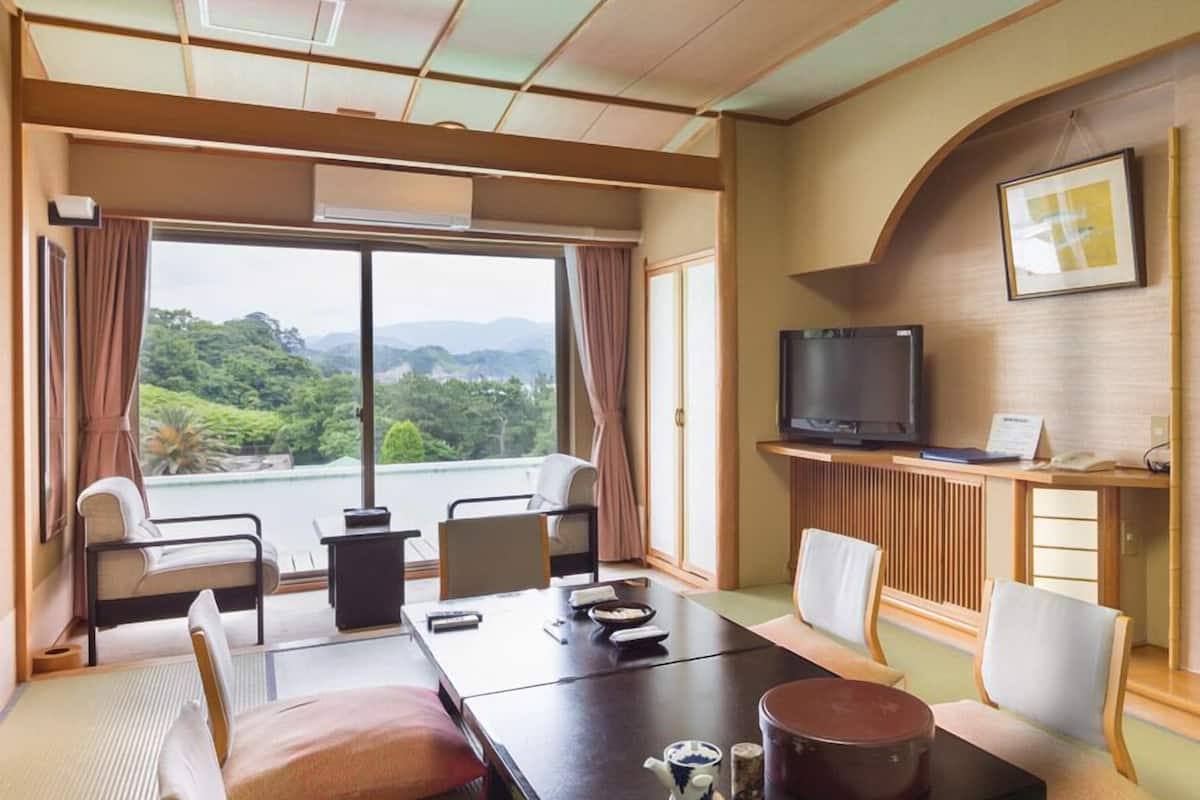 Une chambre d’hôtel dotée d’une grande fenêtre, d’un téléviseur, d’une table à manger et d’un espace de repos aménagé dans le style japonais traditionnel.