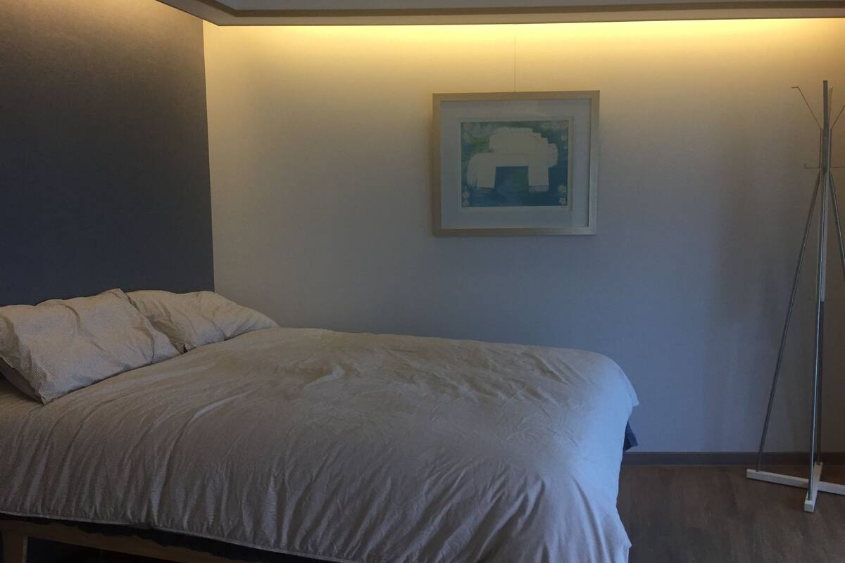 Une chambre à coucher avec un lit, une œuvre d’art encadrée au mur et une lampe sur pied.