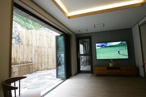 Una sala de estar moderna con un televisor grande montado en la pared, piso de madera y una puerta corrediza de vidrio que da a un patio.