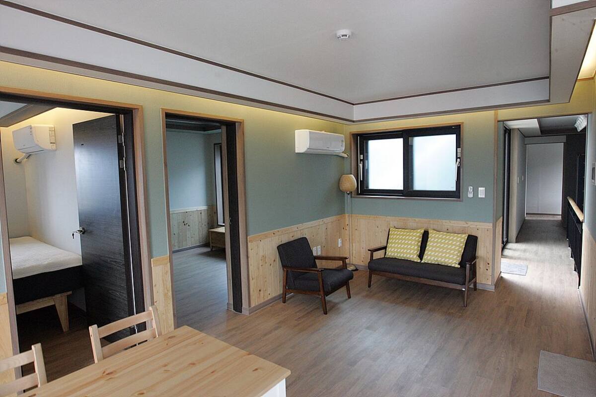 Un espace de vie compact comprenant une table en bois, deux chaises, un canapé avec des coussins à motifs et une fenêtre.