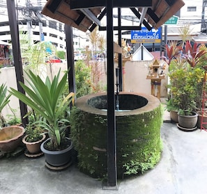 Tipica fontana thailandese con una vasca circolare in pietra, circondata da piante in vaso e un piccolo santuario.