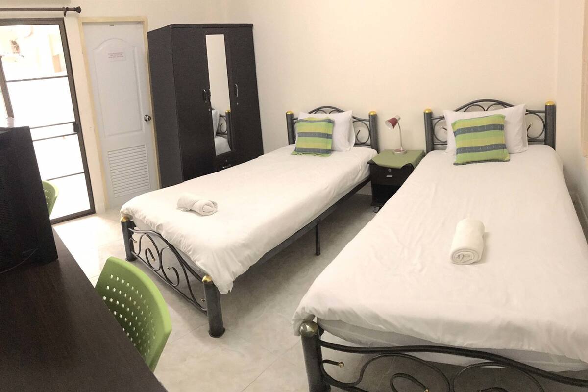 Quarto de hotel com duas camas de solteiro, um guarda-roupa, uma mesa e uma cadeira.
